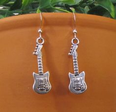 These awesome earrings are perfect for any music lover. Shaped like an electric guitar and crafted from silver-plated pewter and sterling silver 925, they will make a wonderful gift and a great addition to any collection. Earrings feature single-sided Guitar charms on sterling silver ear wires with bead detail. From top of hook to bottom of guitar, earrings are approximately 1-7/8" long. COLOR: Silver MATERIAL: Antique Silver Plated Pewter, Sterling Silver 925. Would you like to add a colorful B Nickel-free Silver Jewelry For Concerts, Silver Nickel-free Music-themed Earrings, Nickel-free Music-themed Jewelry For Concerts, Guitar Earrings, Silver Dangle Earrings, Gift For Music Lover, Sterling Silver Dangle Earrings, Music Lover, Keep Jewelry