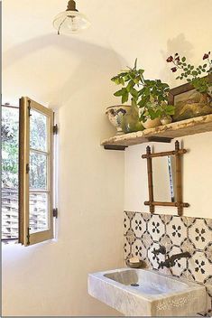 a white sink sitting under a window next to a wall mounted shelf filled with potted plants