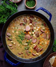 a large pot filled with soup next to some bread and parsley on the side