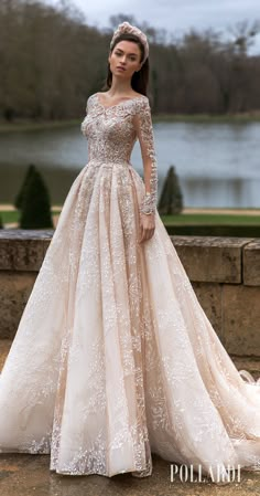 a woman in a wedding dress standing on a stone wall next to a lake wearing a tiara