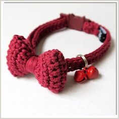 a red crocheted bow tie bracelet with two bells on the end and a bell charm attached to it