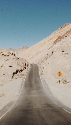 an empty road in the desert with a yellow street sign on it's side