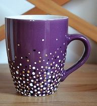 a purple coffee cup with white and gold dots on it sitting on a wooden table