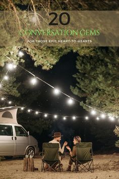 two people sitting in lawn chairs next to a camper with lights strung over it