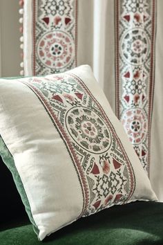 two pillows sitting on top of a green couch next to curtains with red and white designs