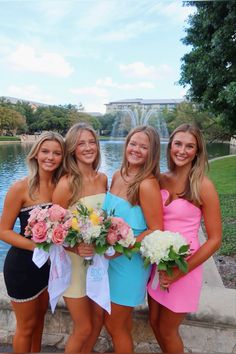 three beautiful young women standing next to each other in front of a fountain holding bouquets