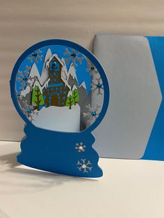 an ornament shaped like a clock tower with snow on the ground and trees around it