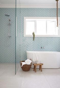 a white bath tub sitting under a bathroom window next to a wooden footstool