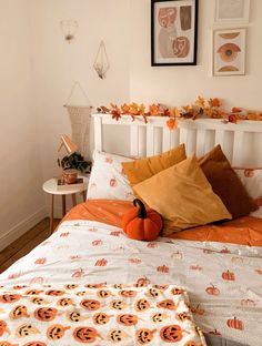 a white bed topped with lots of pillows next to a wall filled with pictures and pumpkins