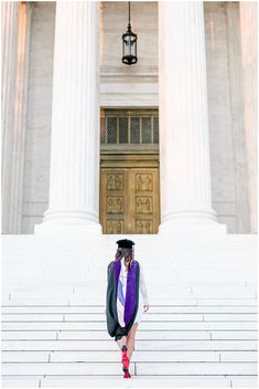 a woman in graduation gown standing on steps with columns and lights above her head, looking at the camera