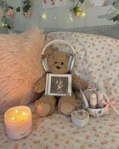 a teddy bear sitting on top of a bed next to a lit candle and other items