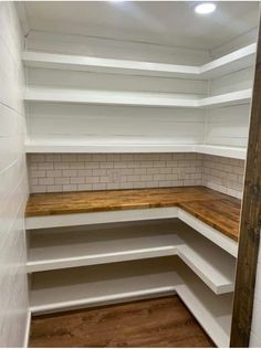 an empty pantry with white shelves and wood flooring on the bottom shelf, next to a brick wall