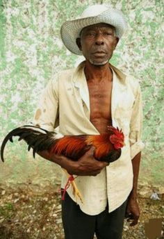 an old man holding a rooster in his hands and wearing a hat on top of his head