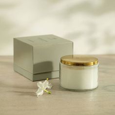 a small white candle with a gold lid next to a box on a table top