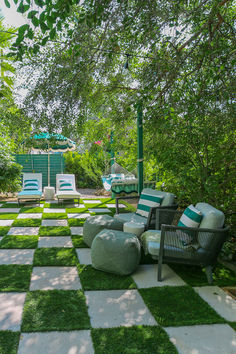 a checkered lawn with chairs and tables in the middle is surrounded by green trees