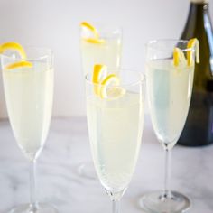 three champagne flutes with lemon wedges in them on a marble countertop next to a bottle of wine