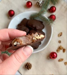 a hand holding a piece of chocolate with nuts in the middle and christmas decorations around it