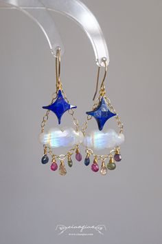 ---- Welcome to CiaoQiao Shop ----- These enchanting earrings feature beautifully crafted blue star gemstones paired with iridescent cloud-shaped moonstones, creating a dreamy and whimsical design. Dangling from delicate gold chains, a selection of colorful gemstones adds a touch of sparkle and elegance, reminiscent of twinkling stars in the night sky. Perfect for adding a celestial touch to your outfit, these handcrafted earrings are ideal for both special occasions and everyday wear. They make a thoughtful and unique gift for anyone who loves the beauty of the cosmos. Please note: natural stones will have flaws and no two stones will look exactly alike. Tips for making your Jewelry last longer - Remove your jewelry before you swim in chlorine or salt water. - Remove your jewelry before p Masc Cottagecore, Star Dangle Earrings, Wire Beads, Colorful Gemstones, Princeton Nj, Twinkling Stars, Twinkle Star, Whimsical Design, Handcrafted Earrings