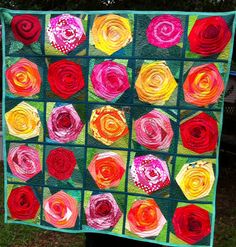 a quilt made to look like flowers with different colors and shapes on it, sitting in the grass