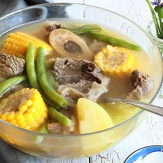 a bowl filled with meat and vegetables next to a plate full of corn on the cob