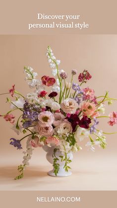 a white vase filled with lots of flowers on top of a table next to a pink wall