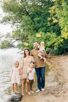 a family standing on the shore of a lake in front of some trees and water