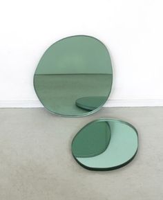 two circular mirrors sitting on the floor next to each other in front of a white wall