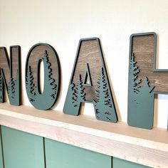 wooden letters that spell out the word aoa on a mantel with pine trees