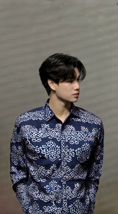 a young man with black hair wearing a blue shirt and jeans standing in front of a wall