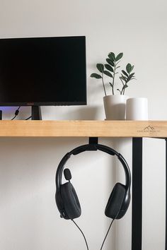 a computer monitor sitting on top of a wooden shelf with headphones hanging from it