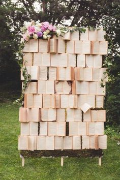 a wooden structure made out of books with flowers on the top and bottom, surrounded by grass