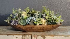 a wooden bowl filled with succulents and greenery