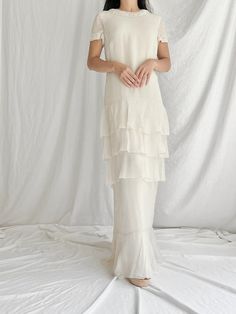 a woman standing in front of a white backdrop wearing a dress with tiered layers