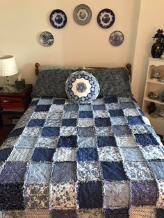 a blue and white quilted bed with plates on the wall above it in a bedroom