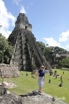 a woman standing on top of a lush green field next to a tall pyramid structure