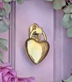 a gold heart shaped door knocker on a purple door with pink roses in the foreground