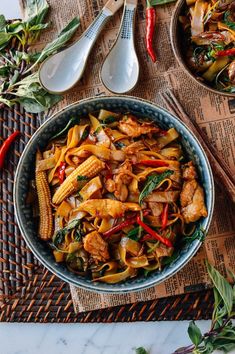 a bowl filled with chicken and veggies next to two spoons on top of a table