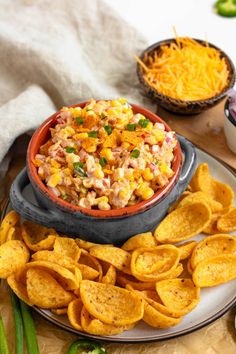 a bowl filled with corn and cheese next to some chips