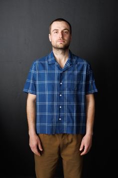 a man standing in front of a black wall wearing a blue shirt and brown pants