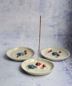 three small white plates with red and blue decorations on them, one has a stick sticking out of it