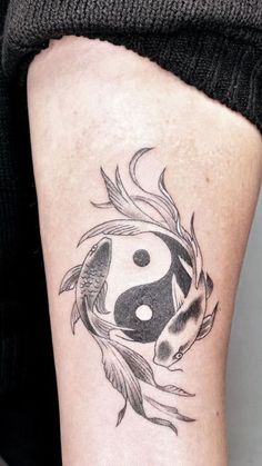 a woman's leg with a yin - yang tattoo on her left thigh and fish in the water