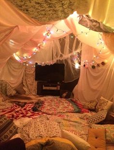 an unmade bed with lights strung from the ceiling and drapes hanging over it