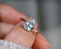 a close up of a person's hand holding a ring with an aqua blue stone