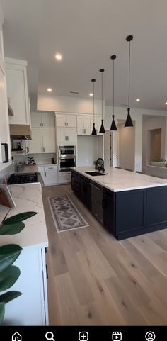 a large kitchen with white cabinets and black island in the center is seen from across the room