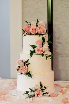 a three tiered wedding cake with pink roses on top and greenery around it