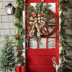 a red front door decorated for christmas with wreaths and deer heads