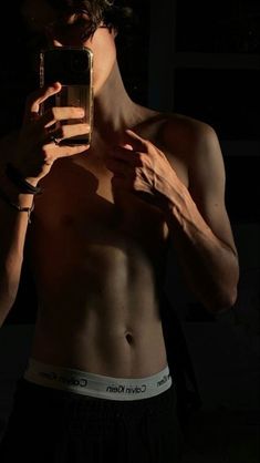 a shirtless man taking a selfie with his cell phone in the dark,