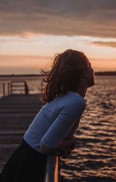 a girl standing on a pier looking at the water with her eyes closed and hair blowing in the wind