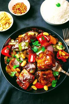 a black bowl filled with chicken and vegetables next to silverware on a tablecloth