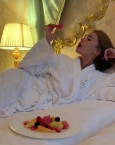 a woman is laying in bed with fruit on the plate and she has her hand up to her head